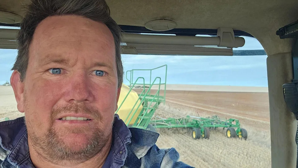 Um homem em um caminhão agrícola com uma colheitadeira ao fundo