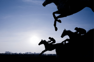 Jóqueis em silhueta montam cavalos de corrida em um salto com obstáculos durante um evento de corrida de cavalos, ilustrando corridas de puro-sangue e esporte equestre contra um céu dramático. Credores de Hawthorne buscam investigação sobre fundos de corrida em meio a um caso de disputa de falência